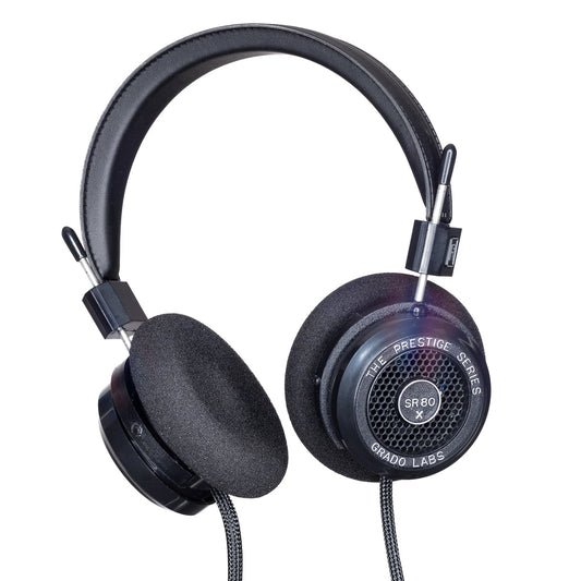 Photo of Grado SR80x Headphones taken from 3/4 view - one ear cup is facing away from view while the other is showing the model name - SR80x - can be seen in the center and the words - The Prestige Series - and - Grado Labs are written on the outside edge of the ear cups. The cables can be seen coming out of the headphone.