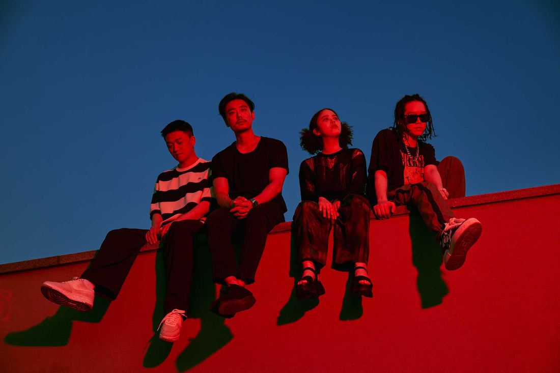 Photo of ADOY sitting on the edge of a bulding withe dark blue sky behind them. Both ADOY and the rooftop are covered in a red light.