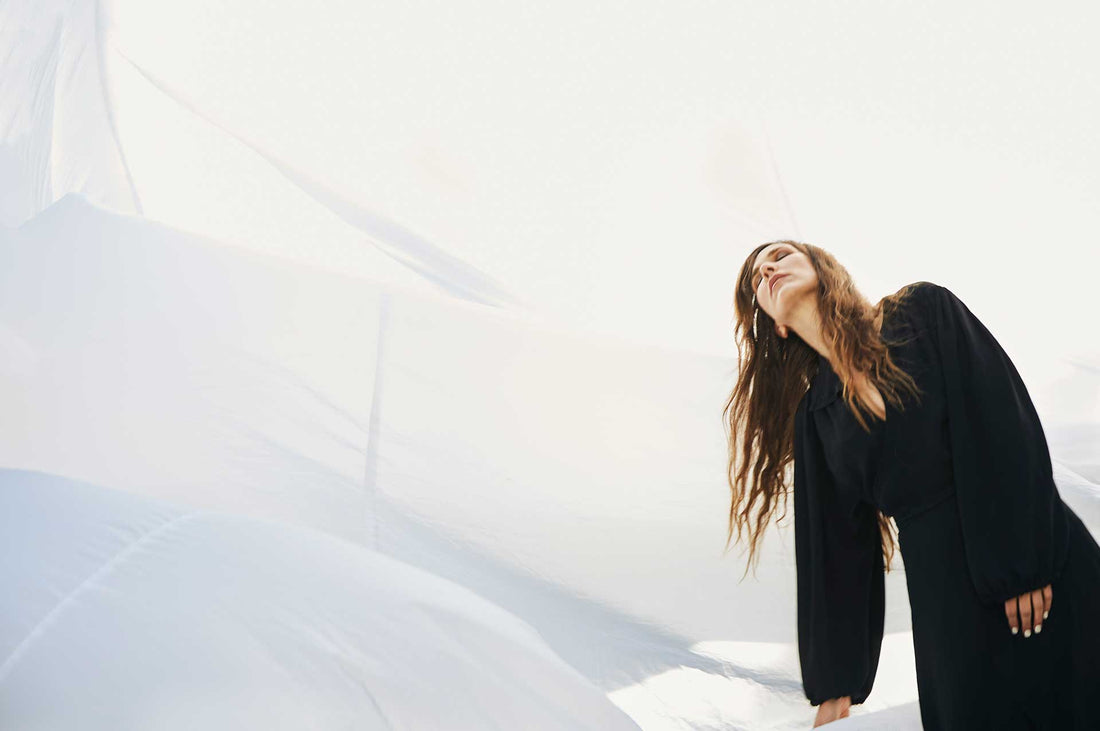 Photo of Reb Fountain in a black dress in front of a large white sheet.