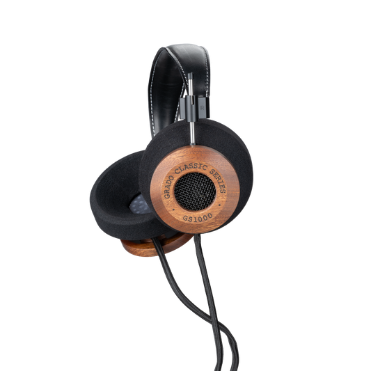 Photo of Grado GS1000 Headphones on a white background taken from the 3/4 view - One ear cup is facing down while the other ear cup is facing outward - the words - Grado Classic Series - and - GS1000 - can be seen on the ear cup.
