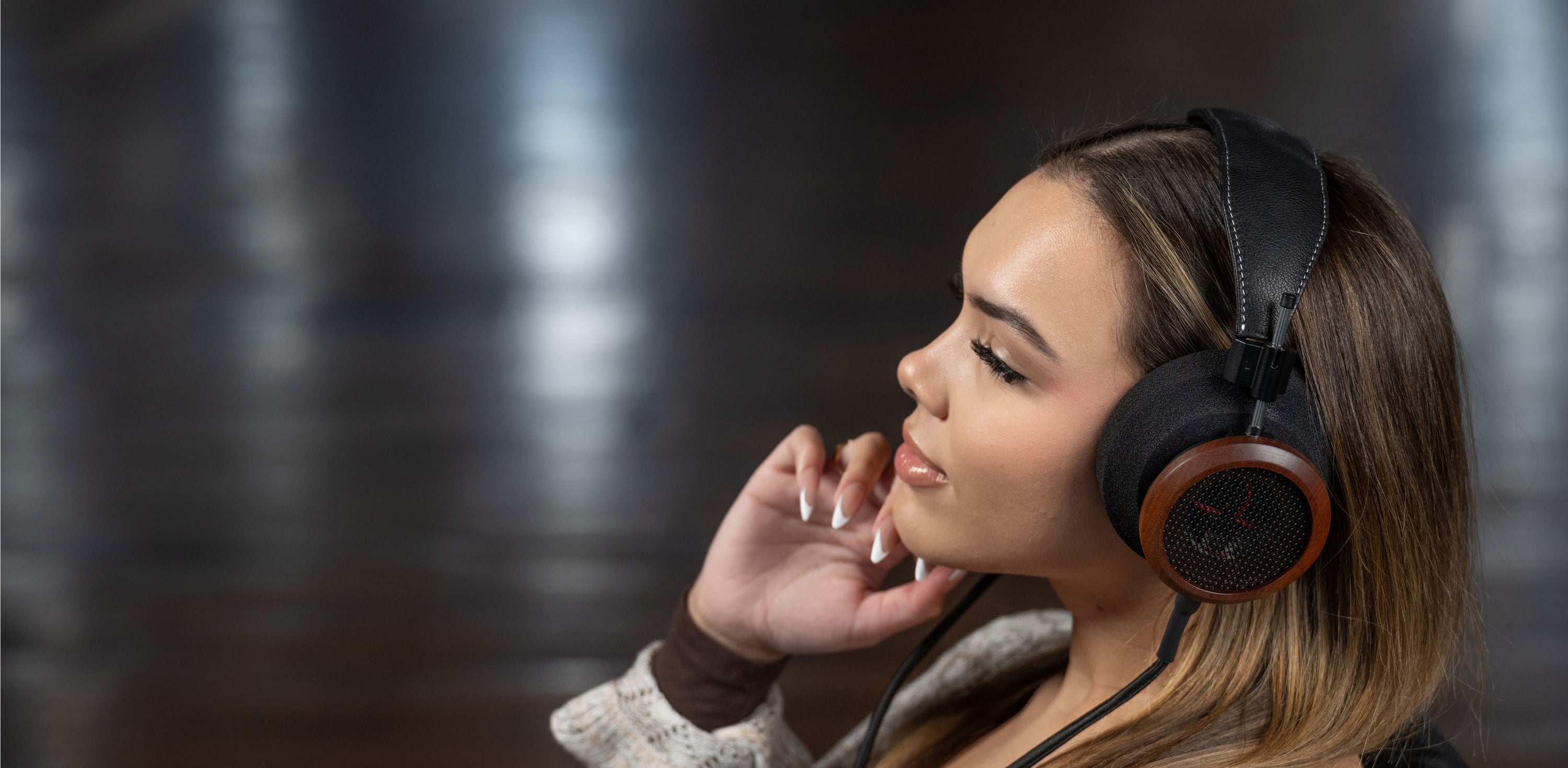 Photo of a woman wearing Grado S950 Headphones while holding her hand on her chin.