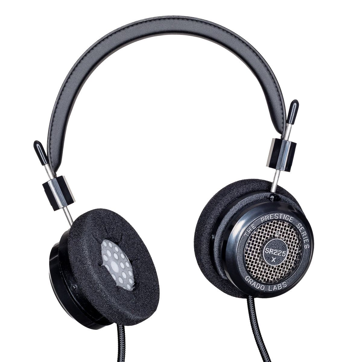 Photo of Grado SR225x Headphones  taken from 3/4 view - one ear cup is facing away from view while the other is showing the model name - SR225x - can be seen in the center and the words - The Prestige Series - and - Grado Labs are written on the outside edge of the ear cups. The cables can be seen coming out of the headphone.