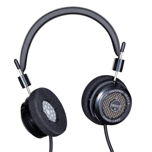 Photo of Grado SR225x Headphones  taken from 3/4 view - one ear cup is facing away from view while the other is showing the model name - SR225x - can be seen in the center and the words - The Prestige Series - and - Grado Labs are written on the outside edge of the ear cups. The cables can be seen coming out of the headphone.